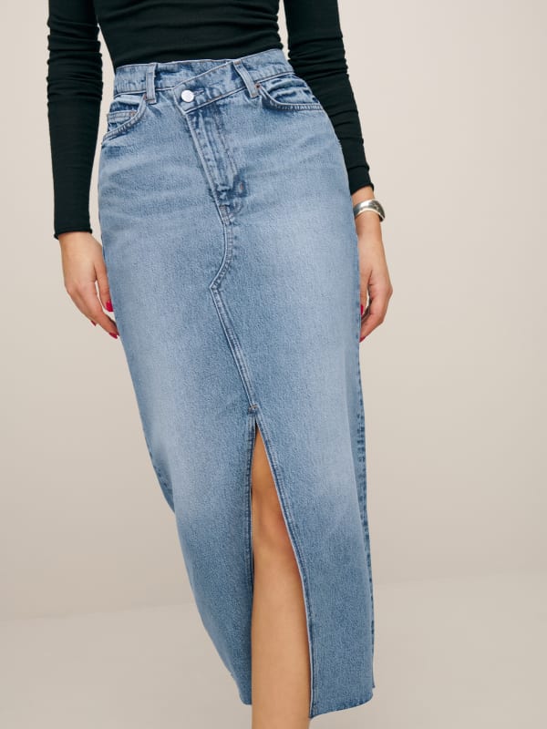 The Reformaiton Nila long denim skirt is a high waisted, midi skirt with a fitted waist, front slit, and a cross over waistband for a little extra shape.