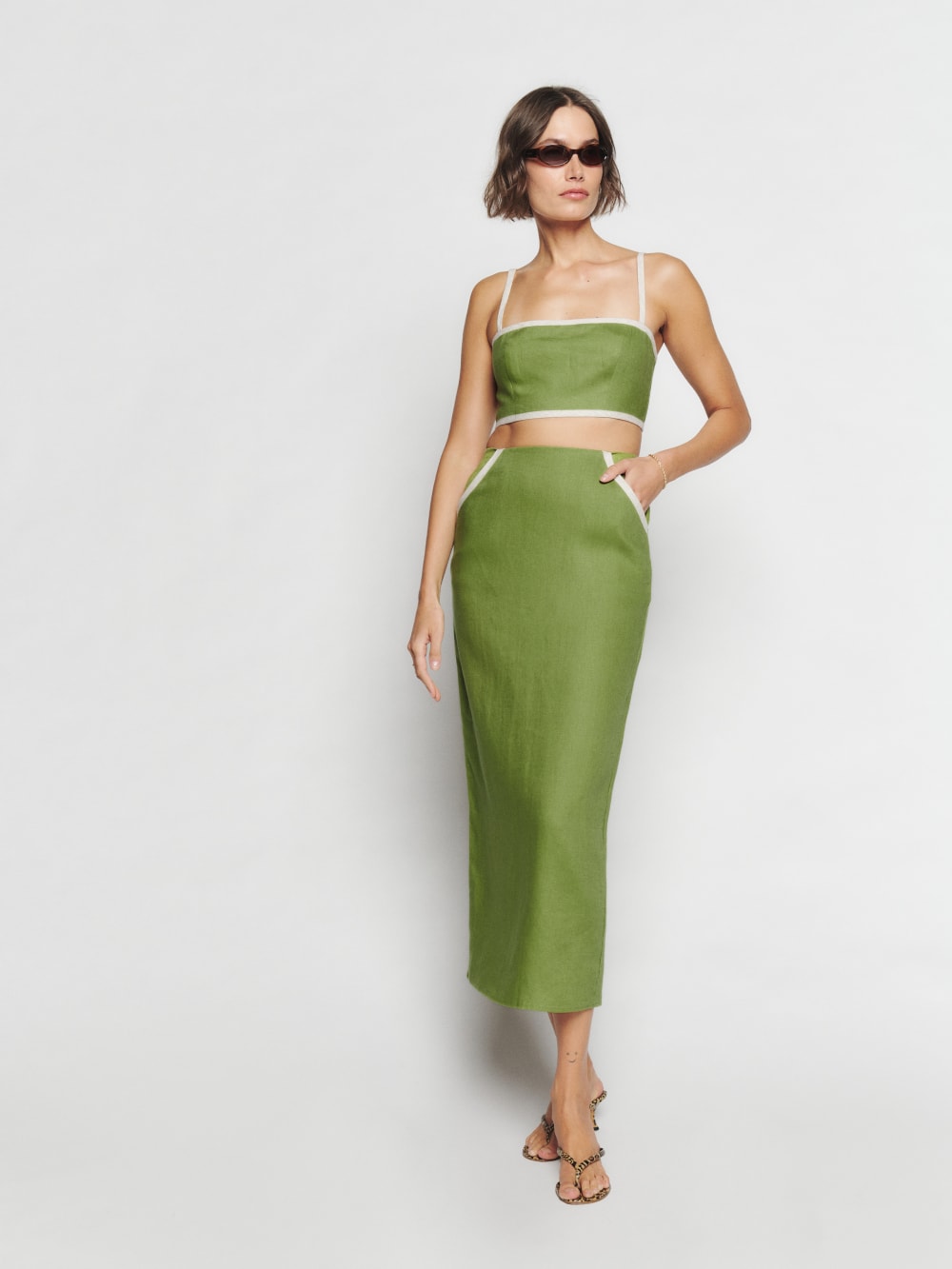 Spice up your summer party looks with Reformation's Elena Linen Two Piece in Avocado Green. It consists of a crop top and linen pencil midi skirt. The top has adjustable straps and straight neckline with white trim detail. The slim fitted skirt has front pockets with white trim detail. 