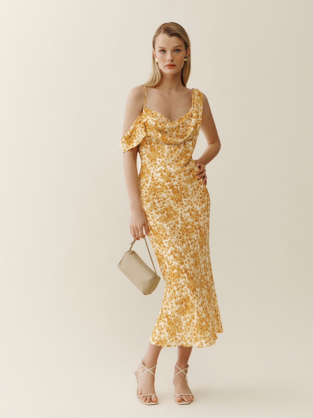 2024 wedding guest outfits - Reformation Reya midi Dress with asymmetric ruffle strap detail is fitted throughout and has a pretty yellow floral pattern. 