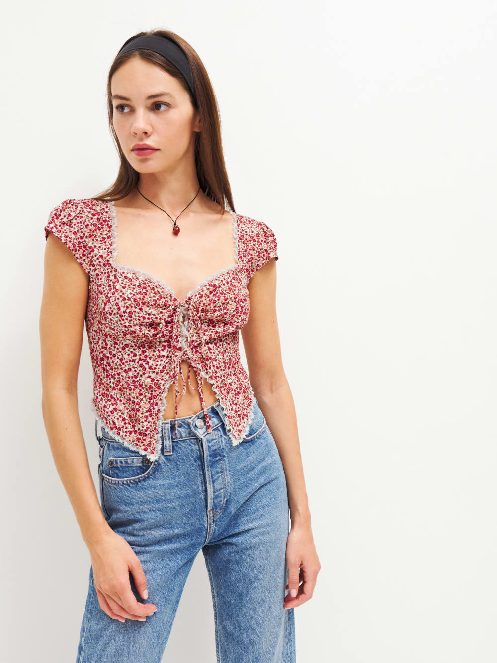 The Reformation safia top is a tie front top in a red floral print with cap sleeves, sweetheart neckline, and peekaboo open midriff. It has a white lace edging. 