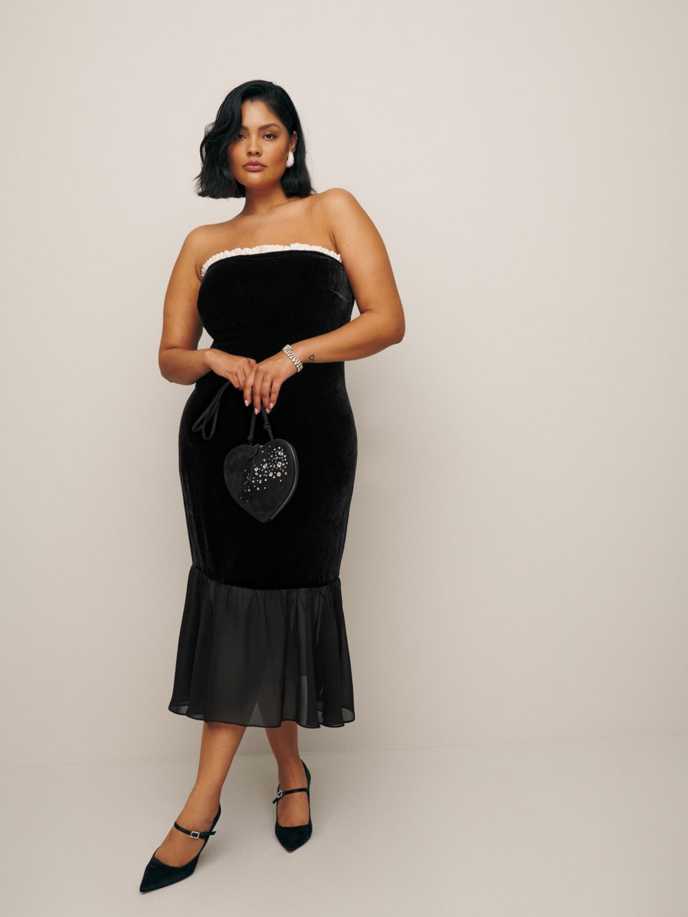 Reformation's Le Marais Velvet bandeau Dress is Designed to be fitted at bodice with a column skirt. It has a Straight neckline with a contrast ruffle in white and a sheer fluted hem. It comes in black soft, non-stretch velvet. 