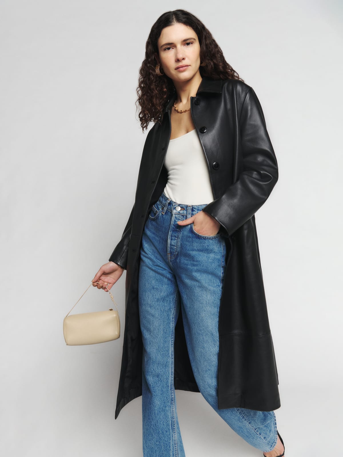 The Reformation Veda leather coat is a black full-length, slim-fit, single-breasted coat. It has functional center-front buttons, so you can wear it both open and closed.