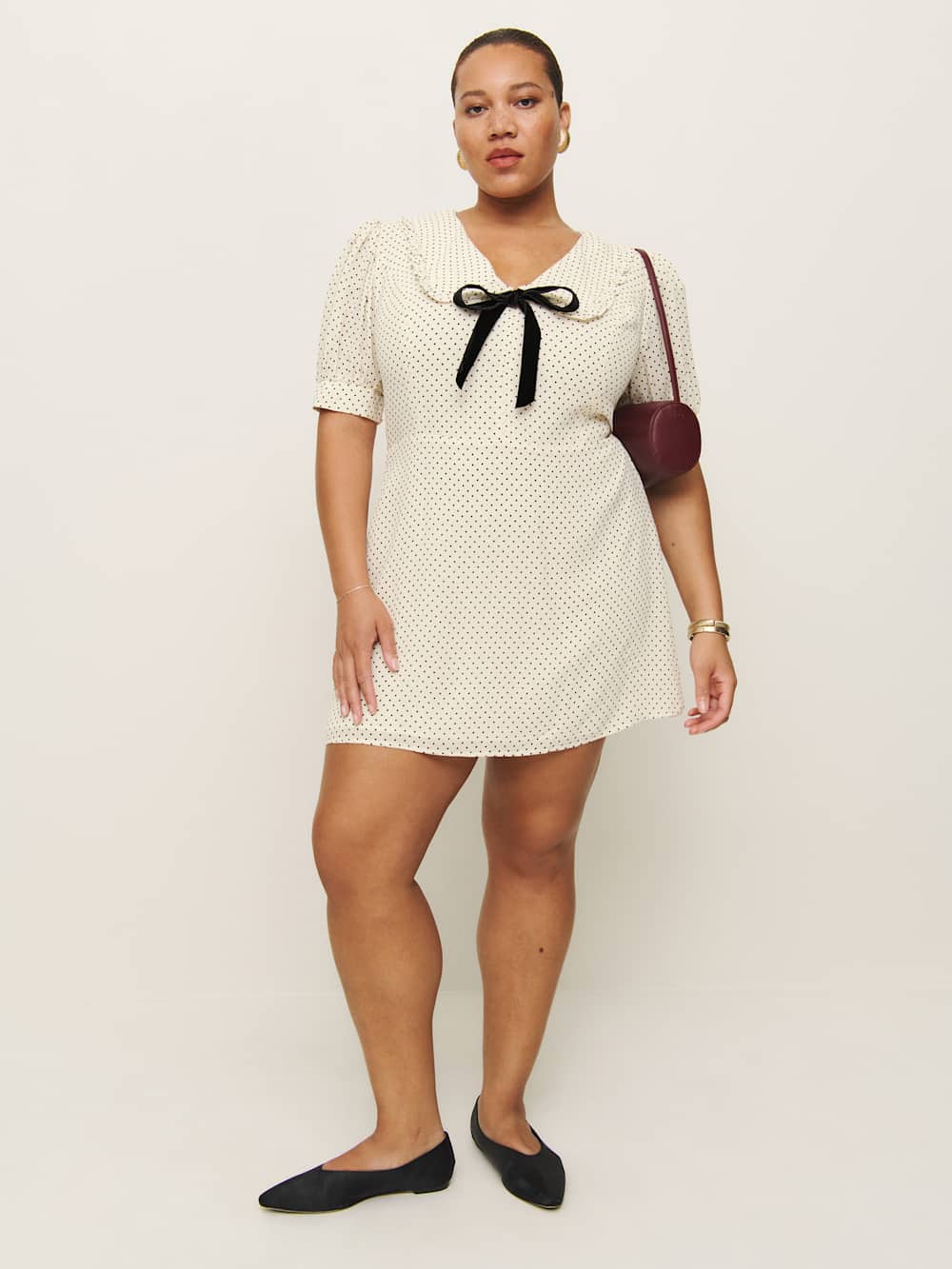 A plus-size, white, collared mini dress with black polka dots and a black bow