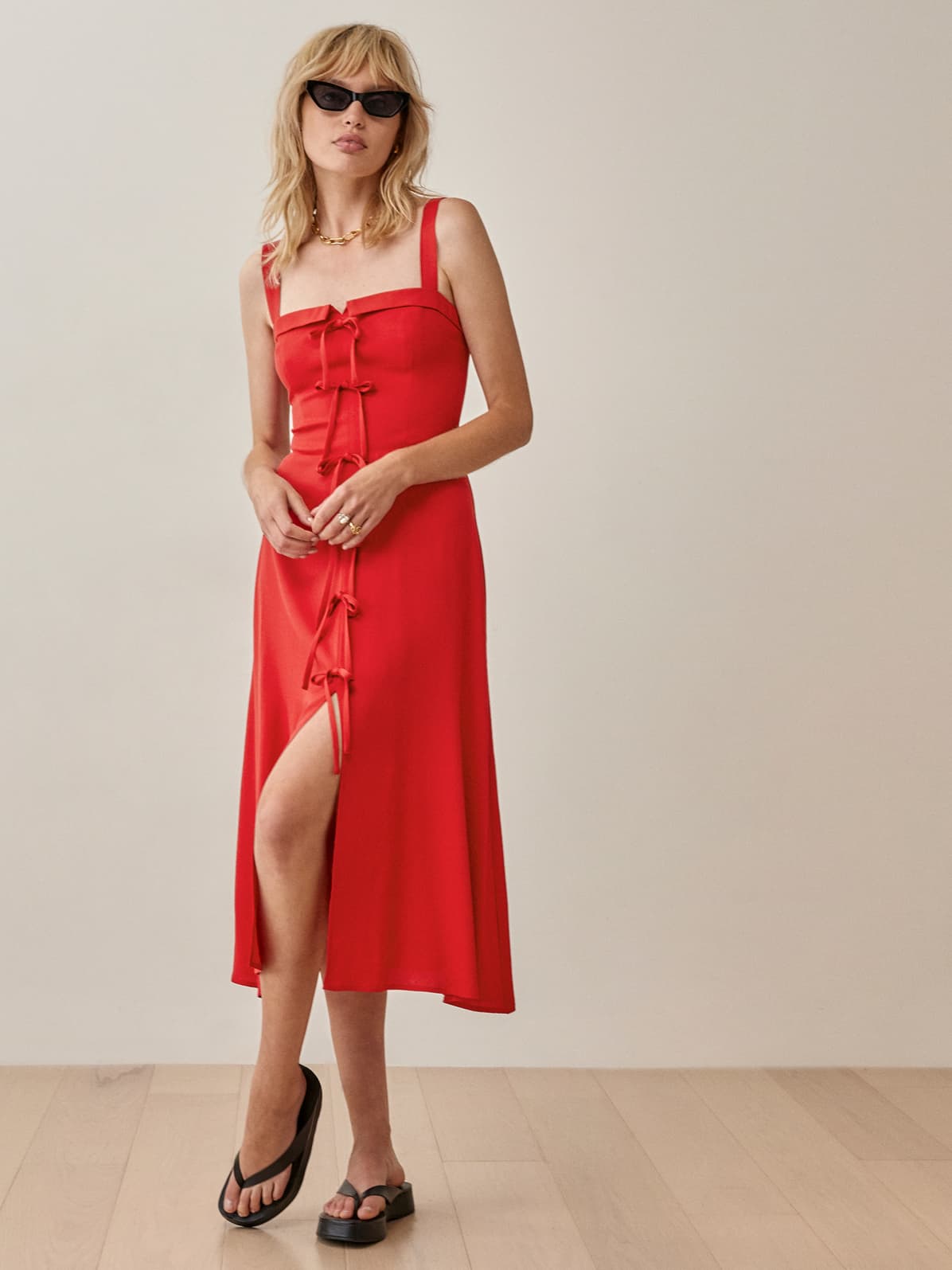 Reformation red Eddie midi Dress with square neckline and thick straps. It skims the body and is detailed with thin sweet bows down the front centre to a slit at the centre of the skirt. 
